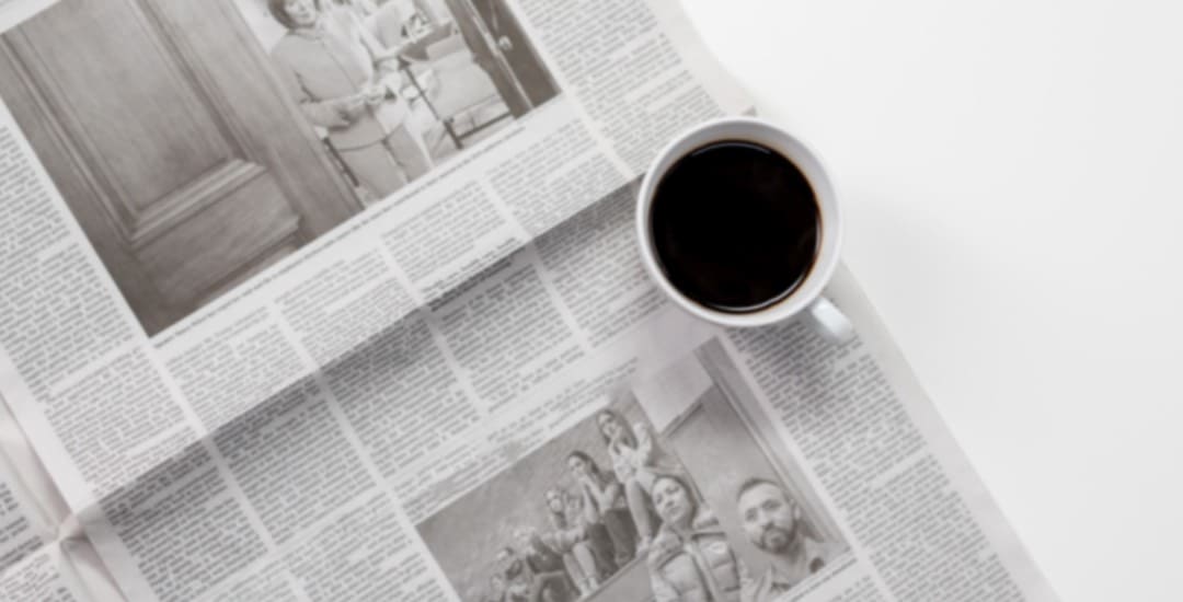 An overhead image of a coffee cup sitting on an open newspaper.