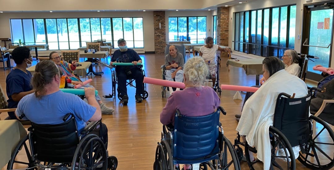 Brickyard Healthcare residents participate in a physical group activity using pool noodles.