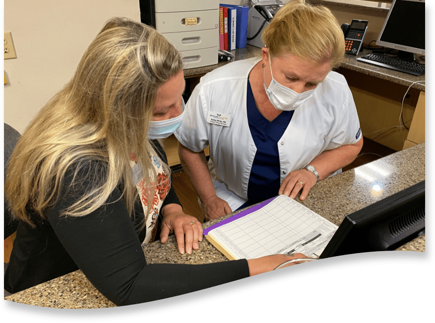 Two members of the Brickyard Healthcare team discuss paperwork at a desk.